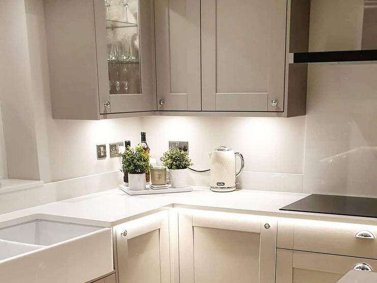 Dove-grey shaker kitchen design with white quartz worktops, silver knob handles, a white Belfast sink and cabinet lights.