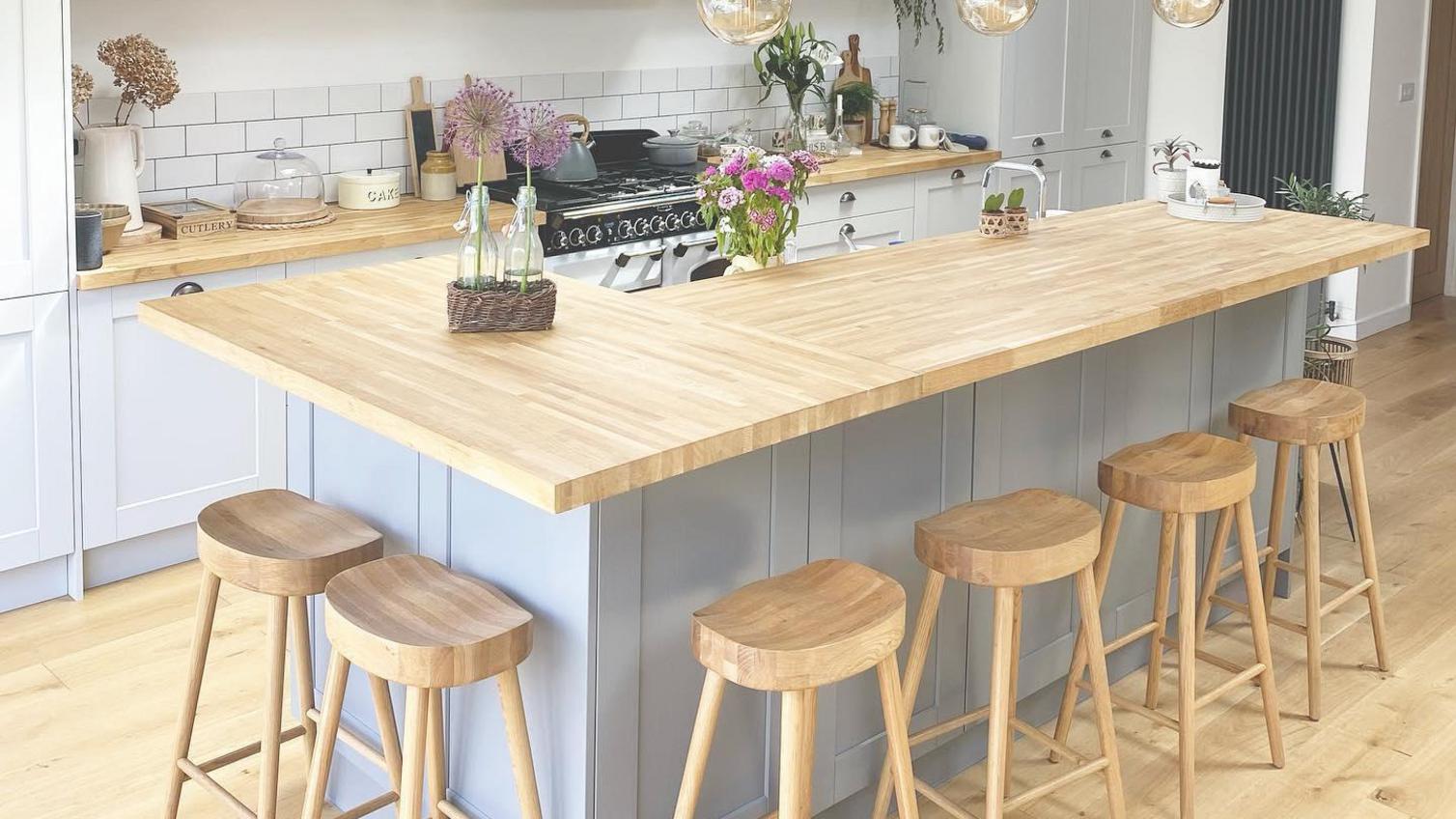 Country kitchen idea with light grey shaker cupboards, an island, oak worktops and matching oak stools.