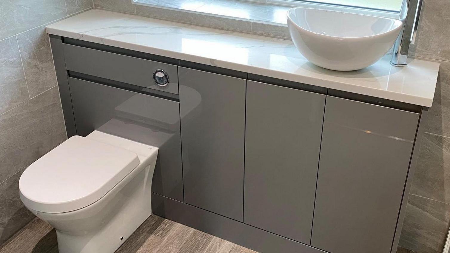 A contemporary bathroom idea featuring glossy grey cupboard doors with an integrated handle design. Includes a white worktop.