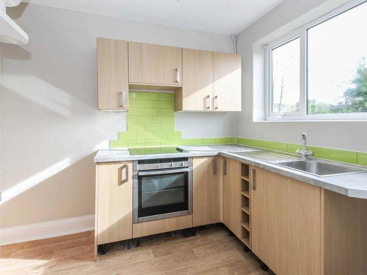 Small L-shaped kitchen with wood-effect cupboard doors and lime green tiles