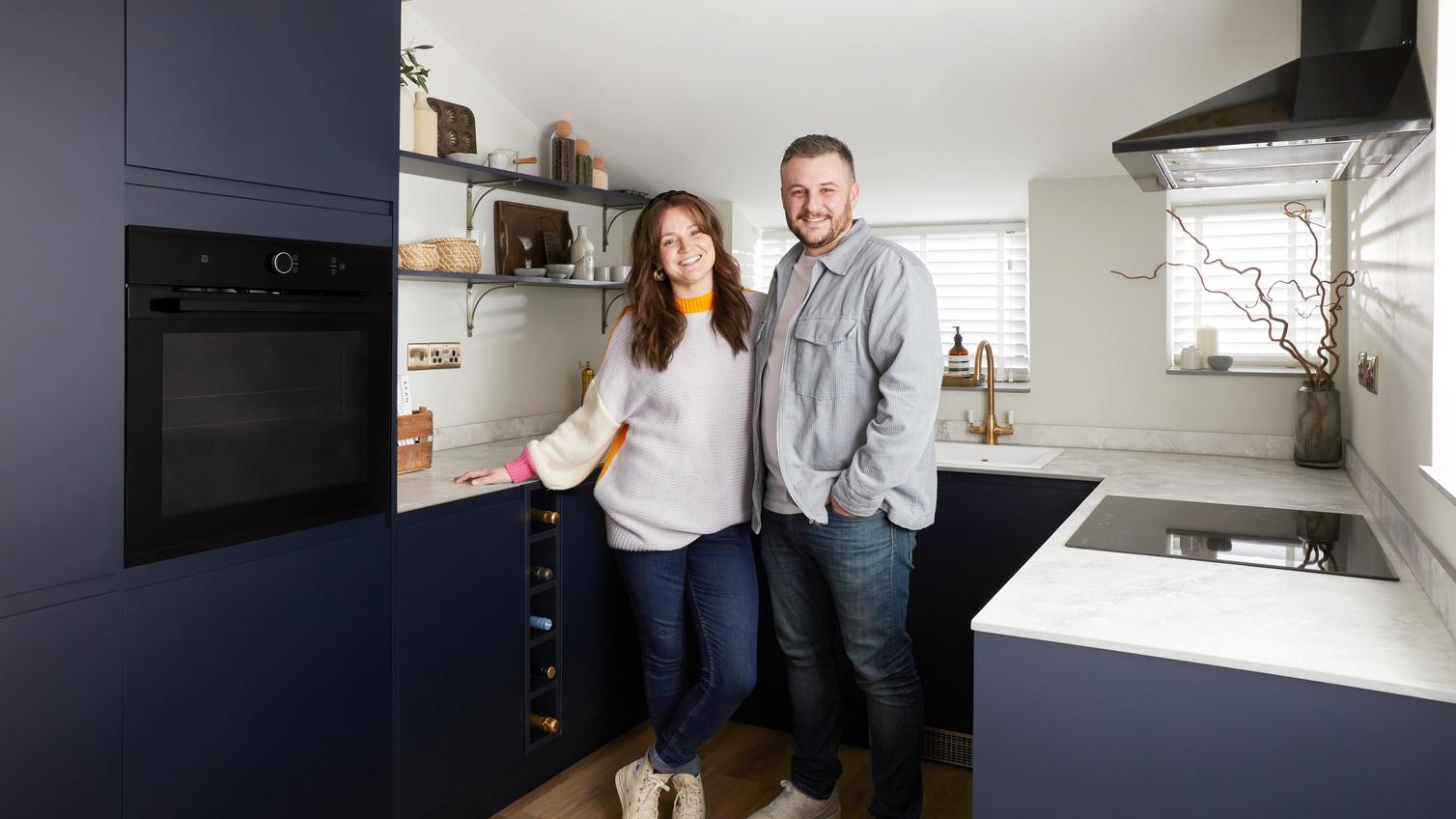 Influencers Grace and James standing in their Clerkenwell matt navy kitchen, with an integrated oven, hob, and extractor.