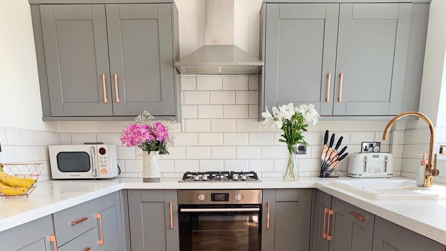Fairford slate grey kitchen with copper handles, an oak chevron floor, white countertops and white subway tiles.