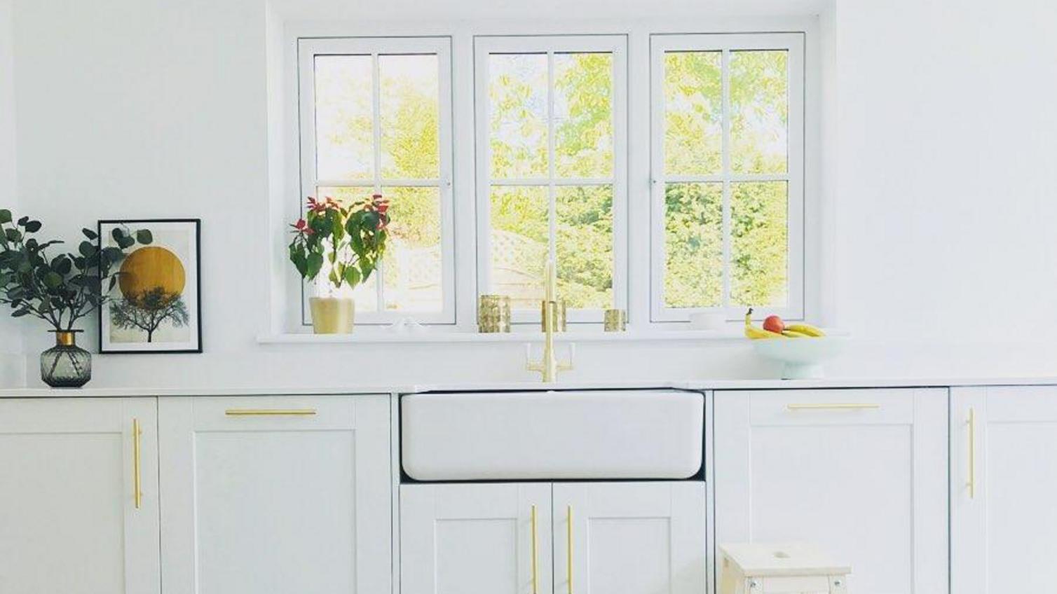 A modern farmhouse white kitchen idea that pairs a ceramic sink with crisp white shaker doors for an updated heritage look.