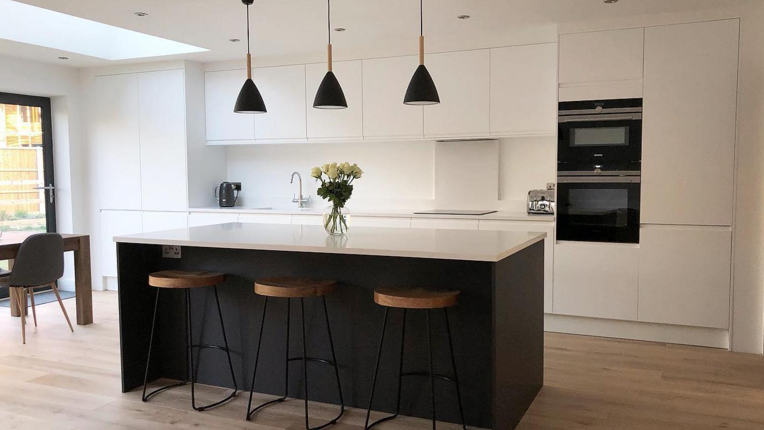 Two-tone black kitchen idea using matt white and black integrated handle doors. Has a dark island and an open plan layout.