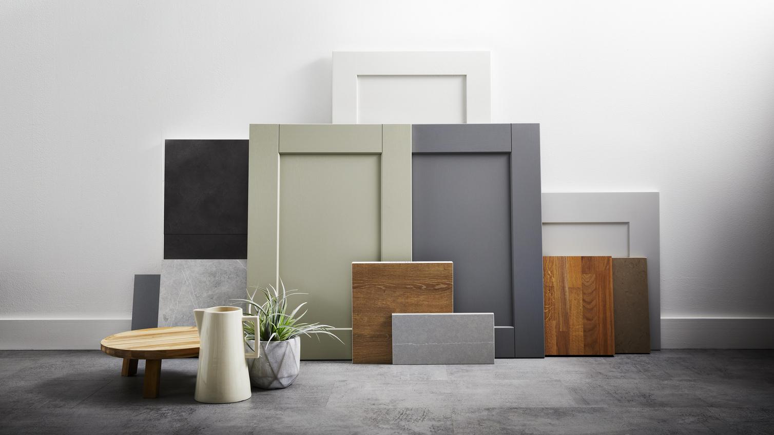 Shaker kitchen doors and boards in natural hues, like green, oak, and white on a grey floor. Propped up against a white wall.