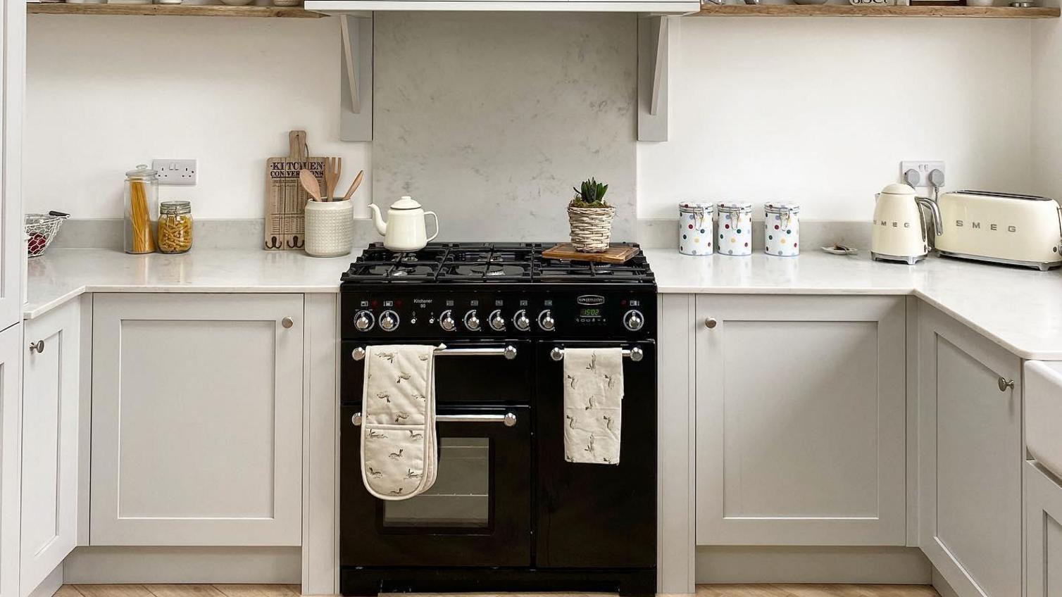 Dove-grey shaker kitchen in a u-shaped layout, with a central hob and open oak shelving.