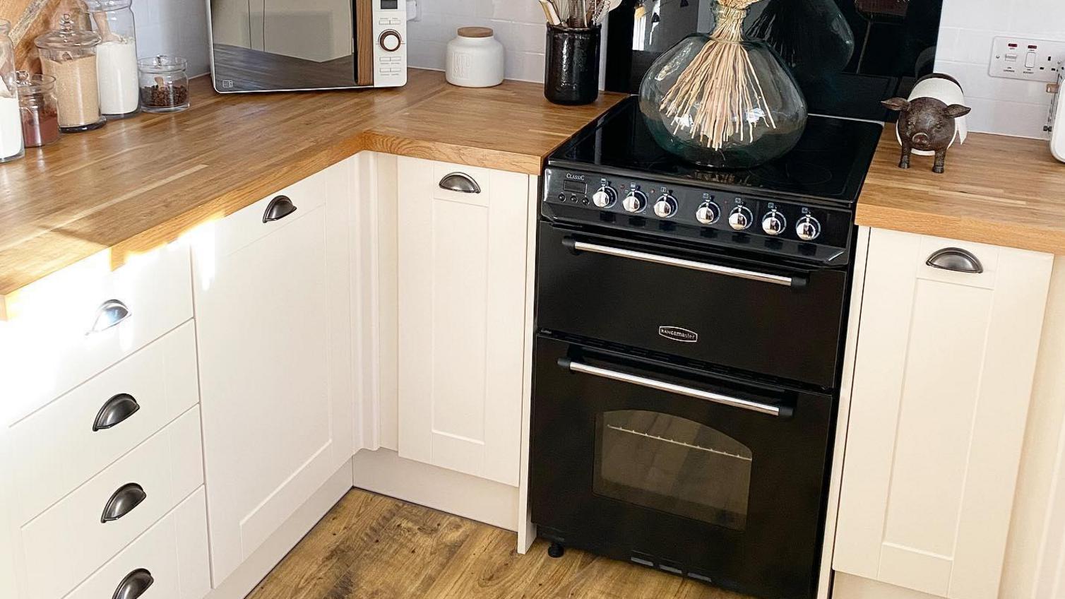 Cream shaker kitchen in a u-shaped layout with brass cup handles, wood flooring and wood worktops.