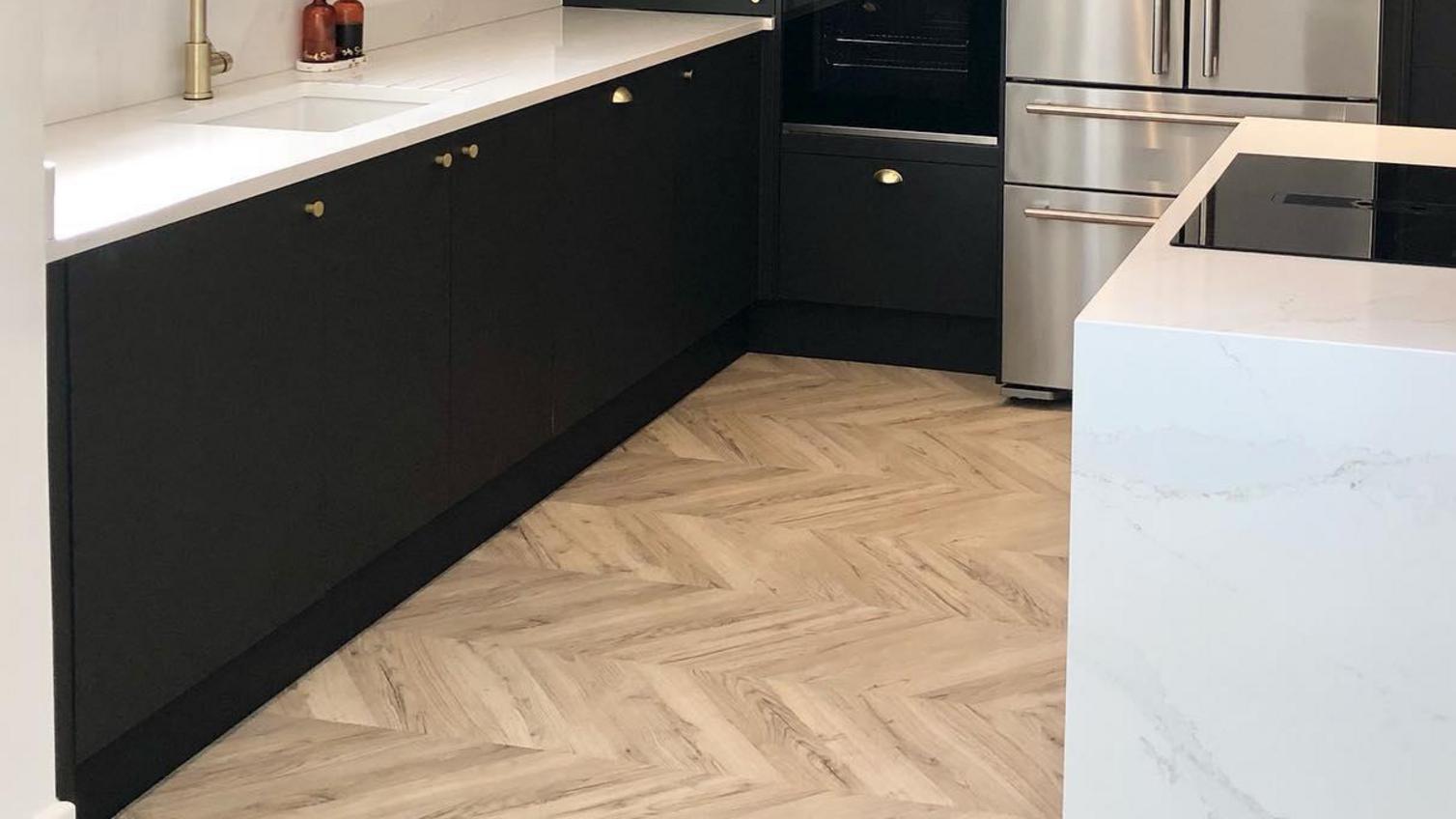 Charcoal slab kitchen design with gold cup handles. white worktops, integrated appliances and chevron flooring.