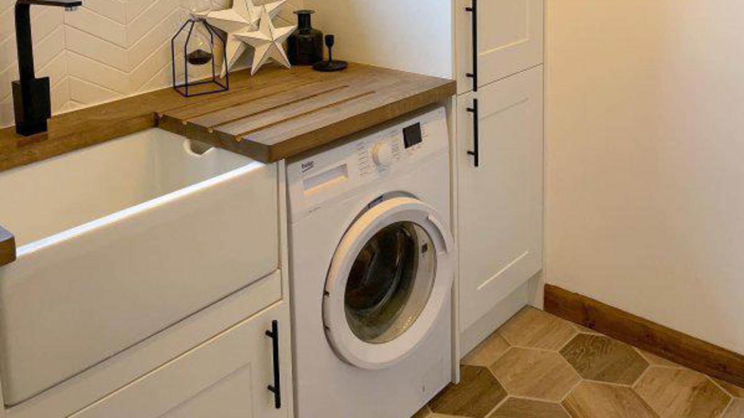 A small utility room in a white colour, with a deep belfast sink, washing machine, and natural timber worktop.