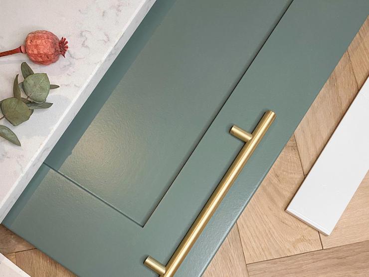 Teal paintable shaker cupboard next to a white marble, with a brass bar handle, pink dried flowers and oak chevron flooring.