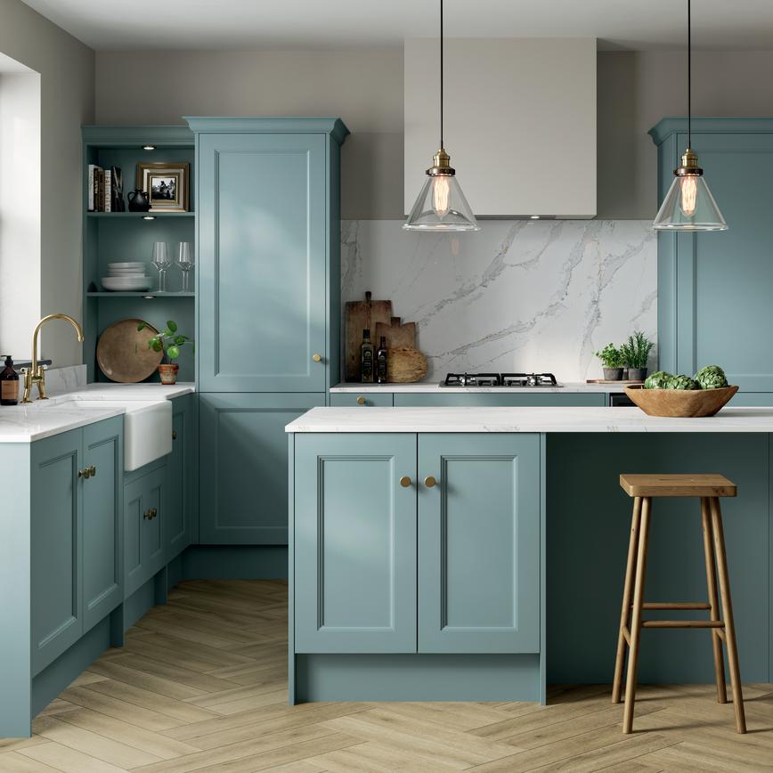 An l-shaped shaker kitchen, with a seafoam blue finish. It has a kitchen island, brass accessories, and oak-style flooring.