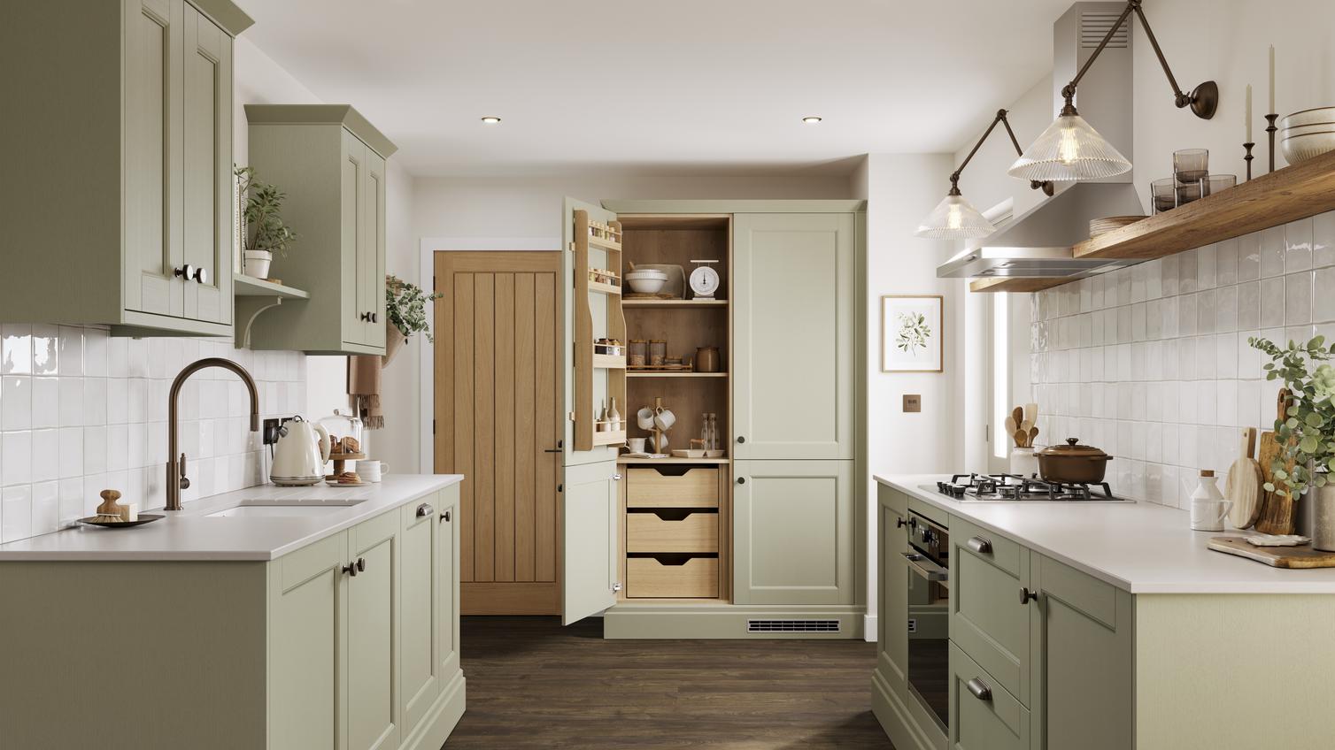 A sage green shaker kitchen with larder unit in a galley layout. It has dark oak flooring and shelving, and white worktops.