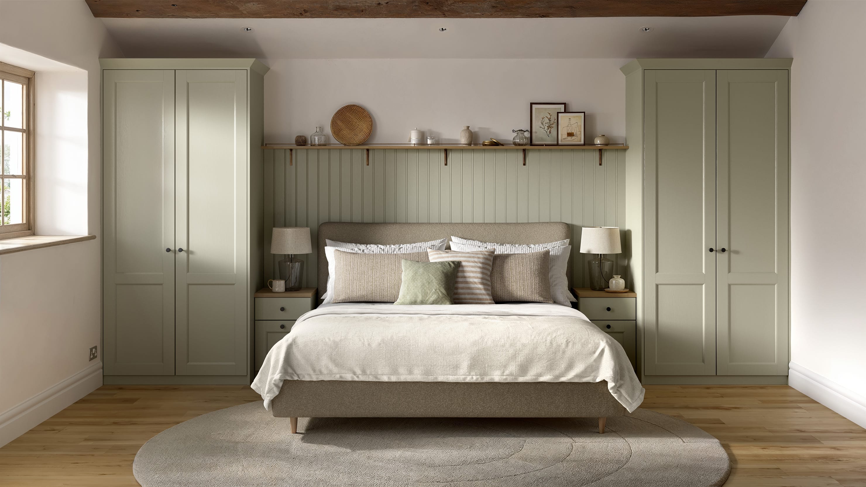 A Bridgemere bedroom with shaker wardrobes in a sage green tone. There is matching, painted wall panels and shelves above.