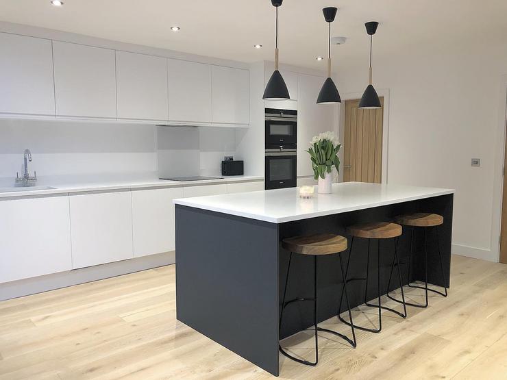 White slab kitchen with a navy island in the centre, light oak flooring and black pendant lights hanging over the island.