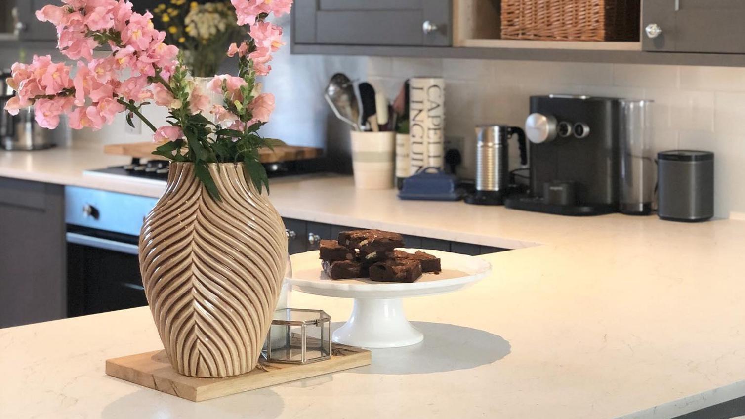 White marble worktop in a breakfast bar layout, with dark grey shaker cupboards, bouquet of flowers and brownies on display.