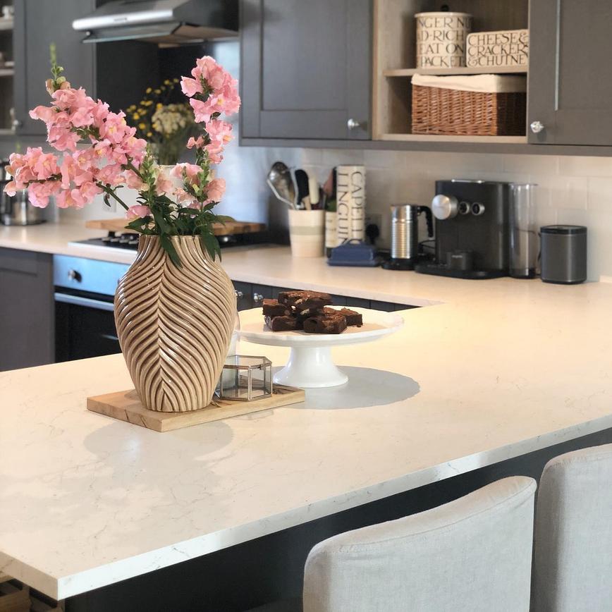 White marble worktop in a breakfast bar layout, with dark grey shaker cupboards, bouquet of flowers and brownies on display.