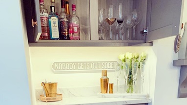 Grey shaker style cupboard used as a barware station, with an open cupboard showing alcohol.
