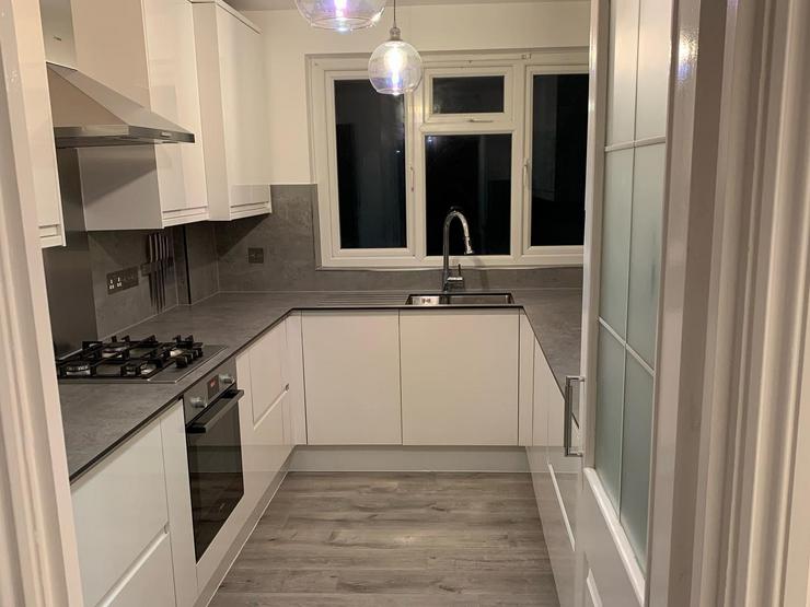 White u-shaped kitchen design with integrated handle, gloss cupboards that are completed with a grey stone-effect worktop.