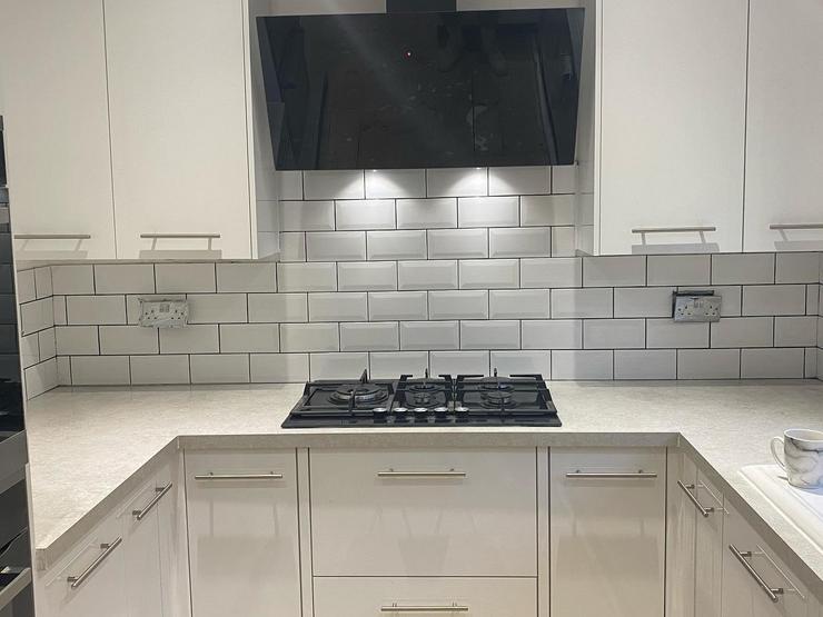 White u-shaped kitchen idea with slab doors, silver bar handles, white subway tiles, black hob and a neutral quartz worktop.