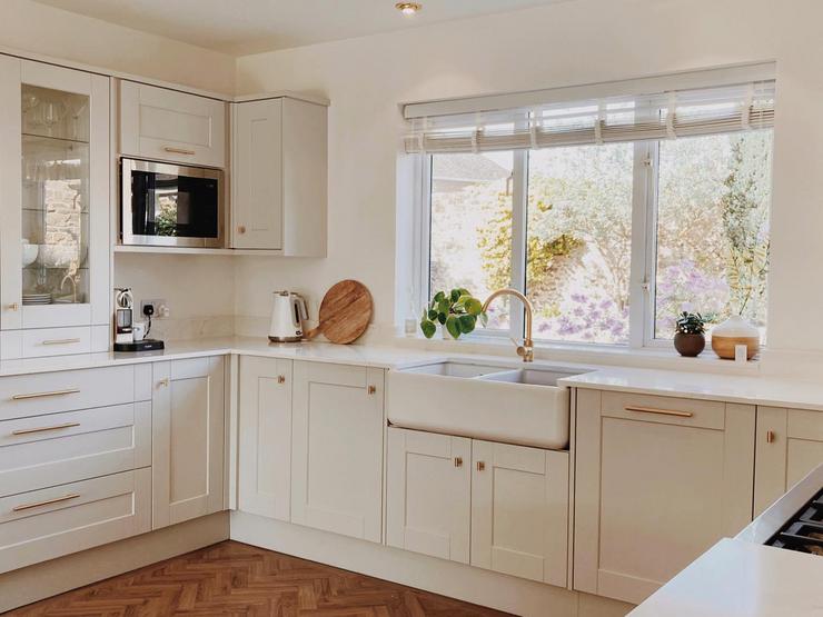 White u-shaped kitchen design with shaker style cupboards, gold handles and tap, white worktops, and a white Belfast sink.