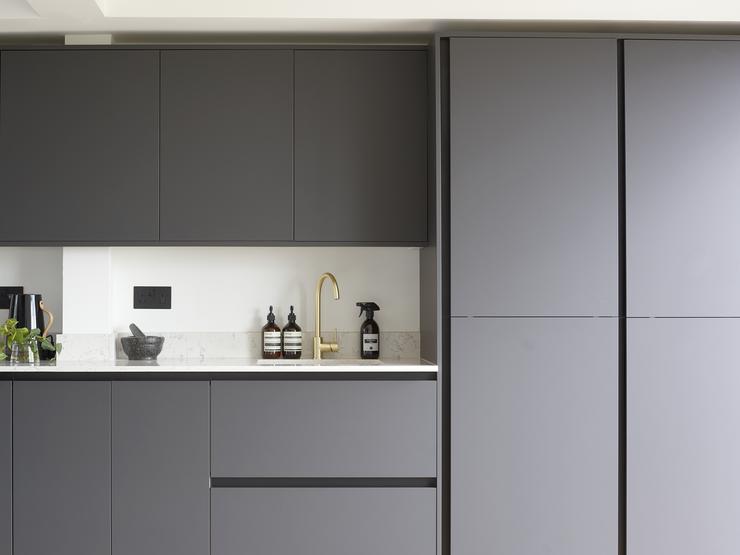 Charcoal grey kitchen design on one wall, with integrated handle matt cupboards, light grey quartz worktop and a brass tap.