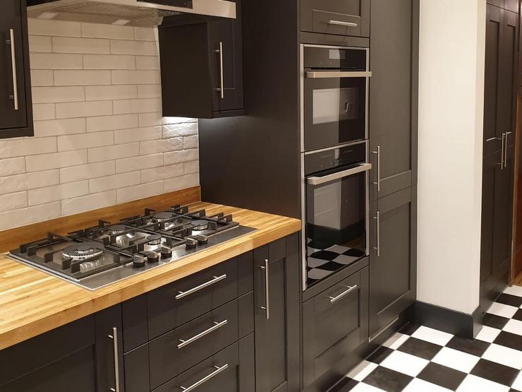 Black shaker style kitchen design with silver bar handles, integrated double ovens, white metro tiles and an oak worktop.