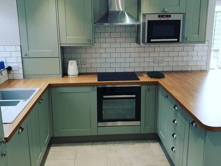 U-shaped kitchen design with green shaker cupboards, a dark oak-effect worktop, white subway tiles and a hob in the centre.