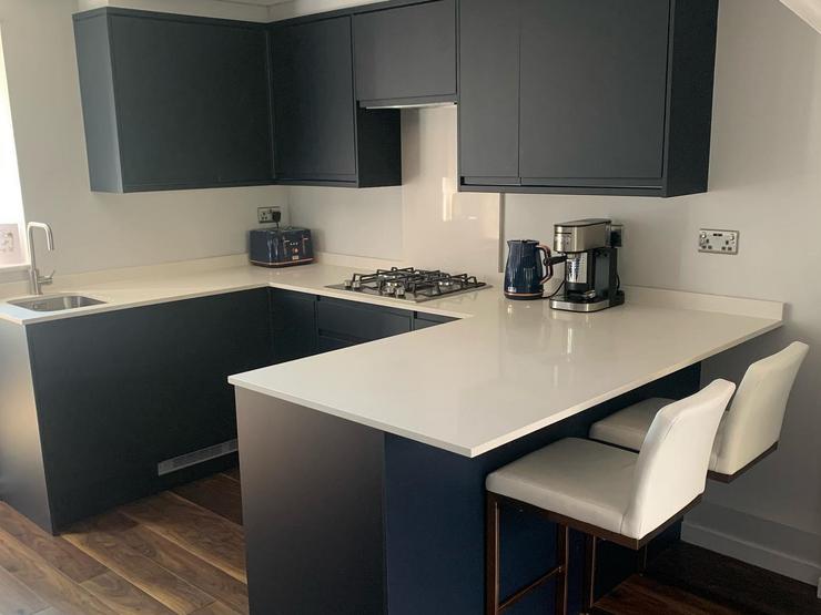 U-shaped kitchen design with navy integrated handle cupboards, a white worktop and a breakfast bar with two white seats.