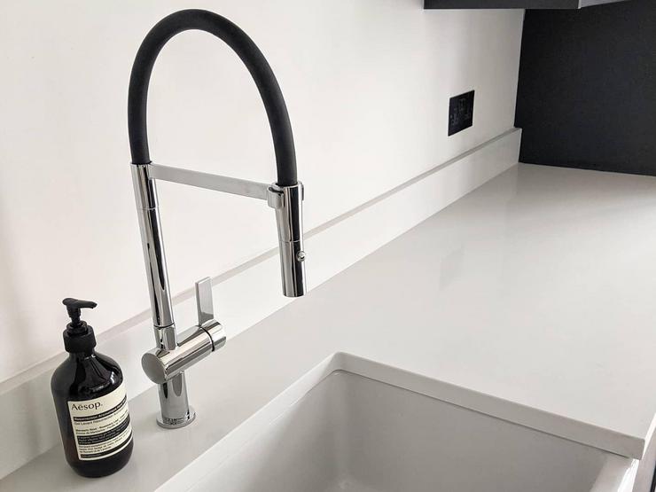 Black and stainless-steel mono mixer tap, with a pull-out hose function, white Belfast sink, and a black bottle of soap.