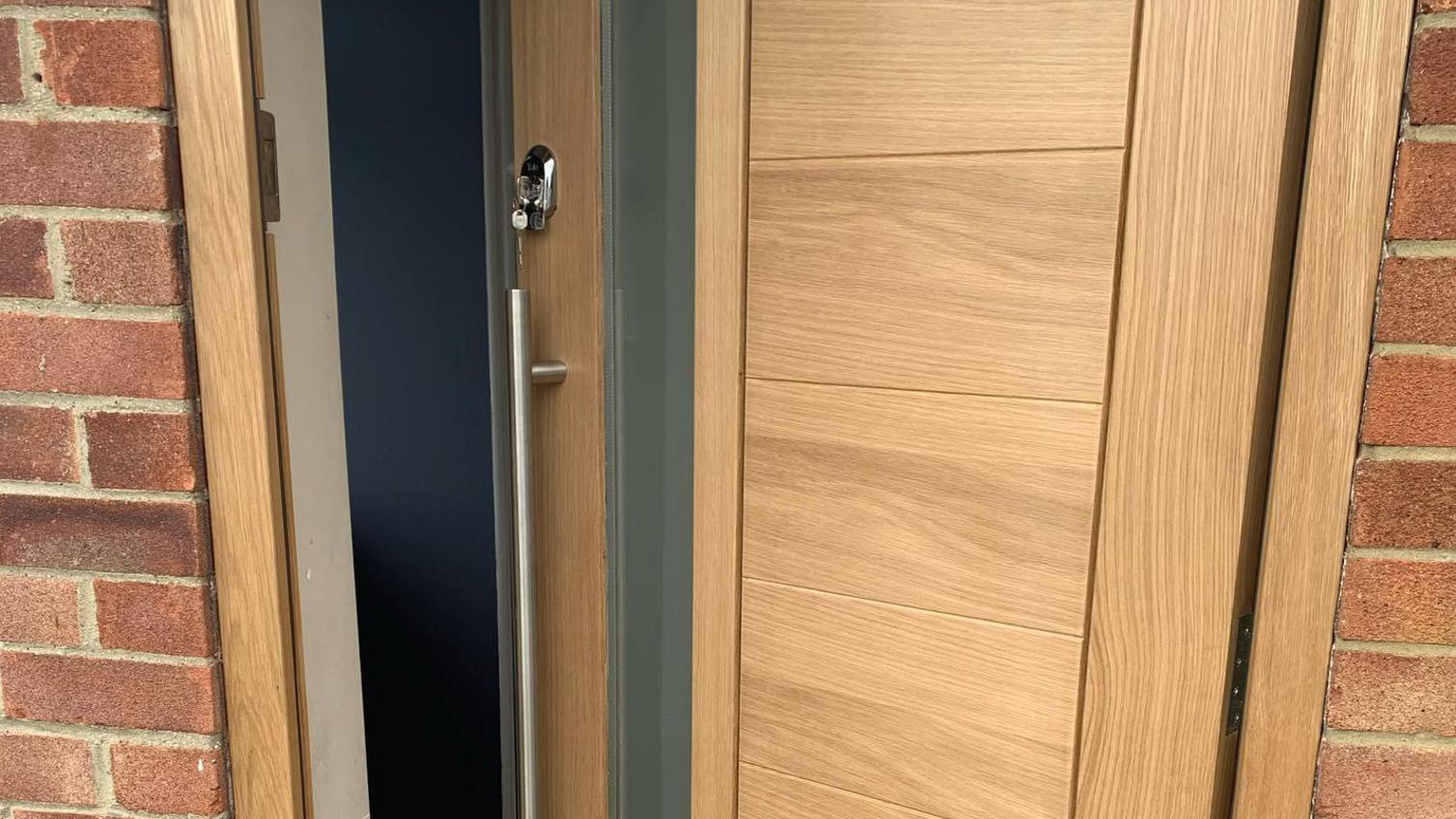 Oak panelled door with long frosted glass panel offering a linear look, with silver bar handle, lock, and a silver letterbox.