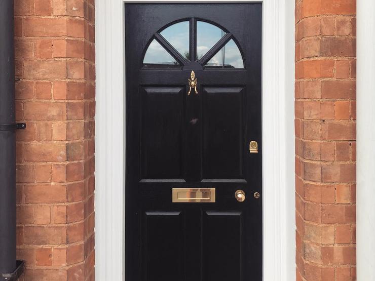 Black four-panelled door with curved glass panels at the top, brass letterbox, knocker, and knob handle, and a white frame.