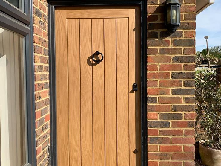 Oak panelled door with five long vertical panels, a black frame and matching black circle knocker, letterbox and handle.