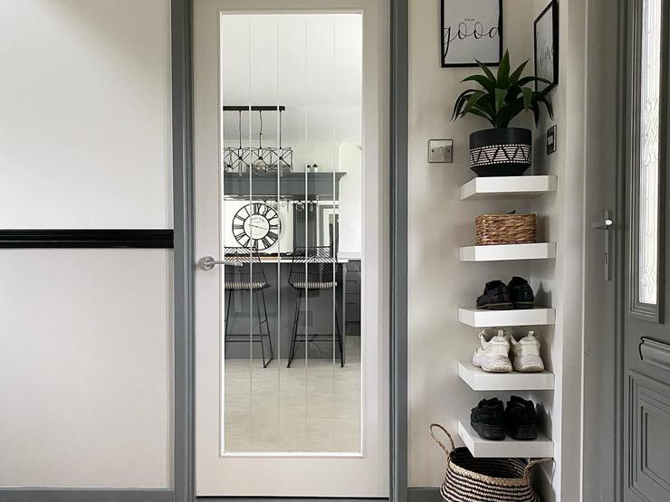 White internal door with a clear glass panel, grey painted frame, white open shelves, and light oak flooring.