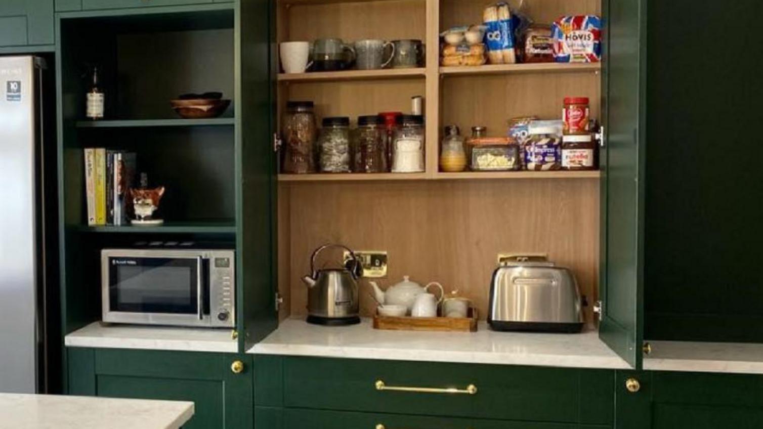 Kitchen storage idea using integrated shelves and matching doors for a hidden breakfast area.
