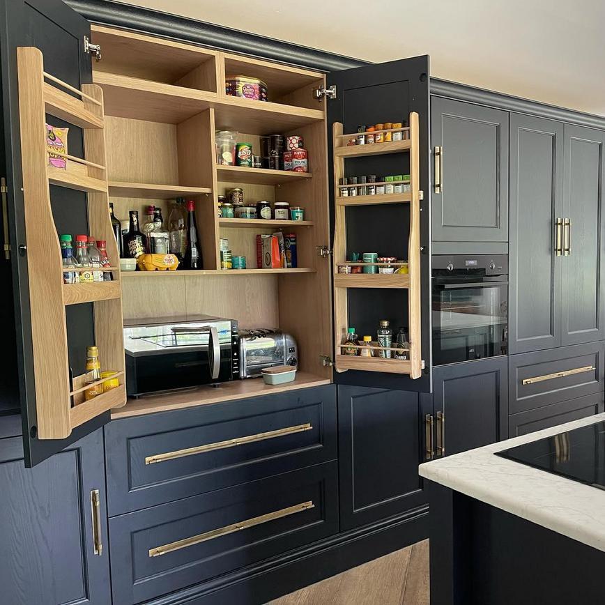 Elmbridge navy kitchen larder cabinet with oak shelves containing food and appliances