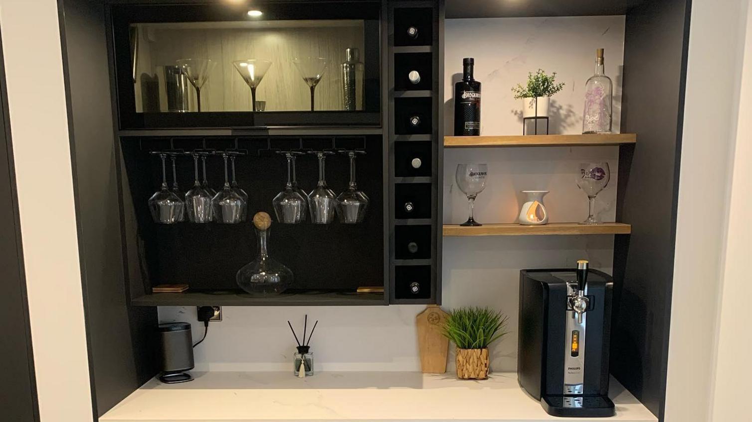 At-home bar idea with dark navy handleless doors, a white marble worktop, and open shelving showing wine glasses.