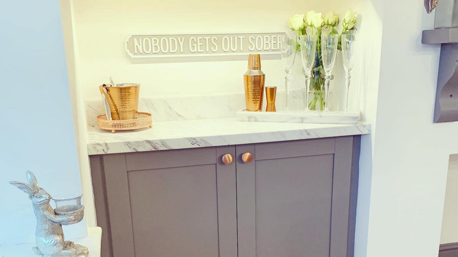 Grey at-home bar idea with copper knob handles, shaker style doors and a marble-effect worktop.