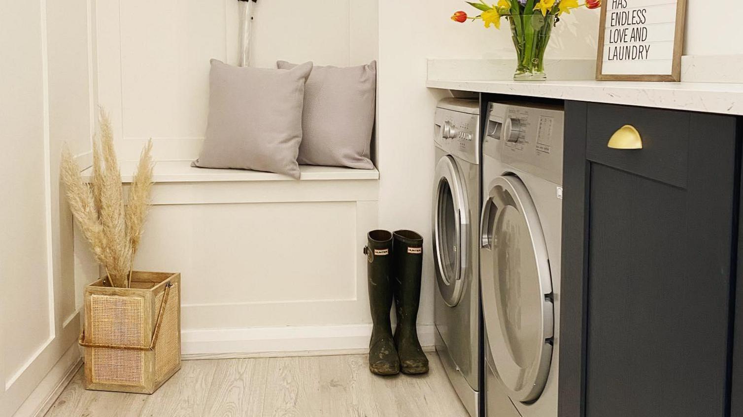 Utility room storage idea showing appliances and navy cupboards, with a storage seat and wall pannelling in ivory.