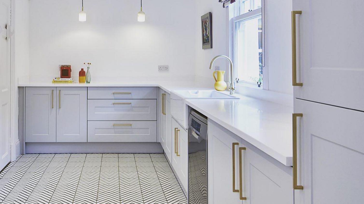 Large utility room idea with light-grey shaker doors, white worktops, gold bar handles and chevron tile floors