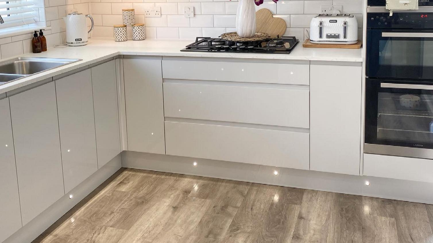 White gloss kitchen with wood-effect flooring and plinth lighting