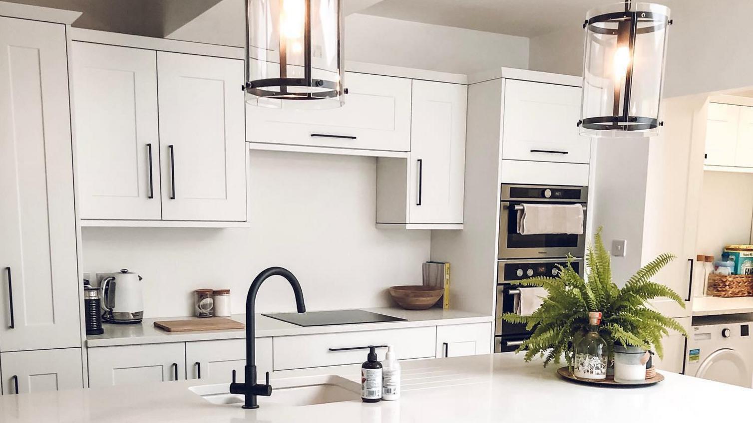 White shaker kitchen idea with black bar handles, an island, white worktops, and matt black tap.