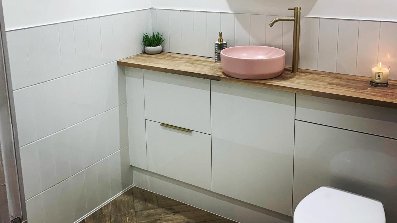 A modern grey bathroom idea using glossy slab cupboard doors. Includes an oak worktop, slimline handles and a timber floor.