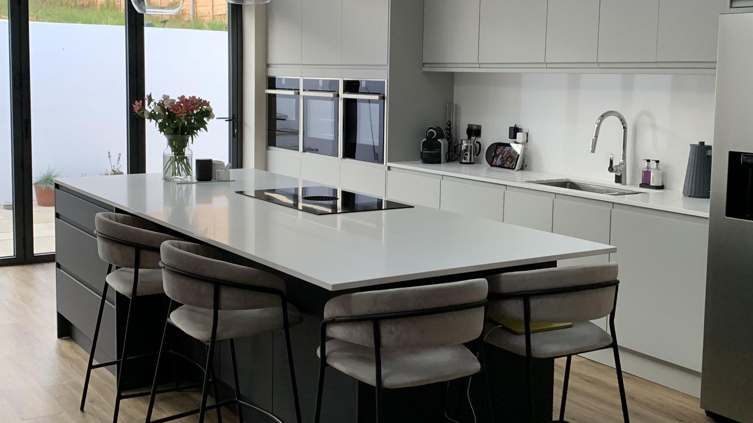 A modern two-tone kitchen idea using white and grey integrated handle cupboard doors in a glossy finish and an island layout.