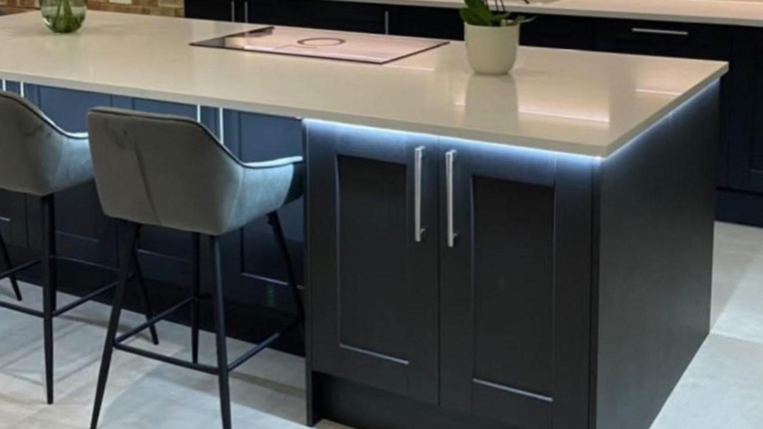 Fairford charcoal black kitchen island with matching base cabinets and dove grey wall cabinets. The island has a quartz worktop.