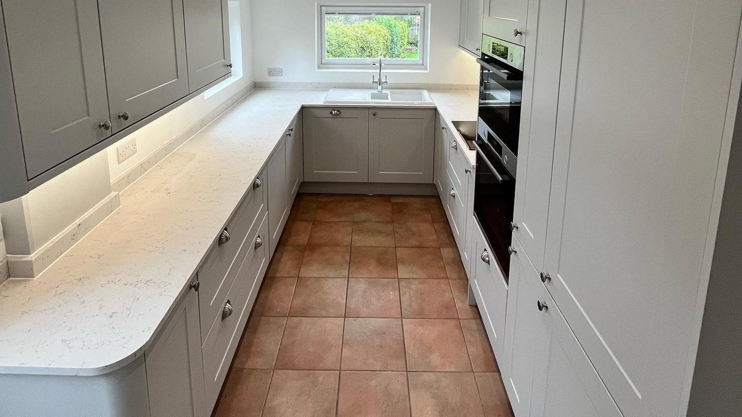 Chelford dove grey shaker kitchen, with white worktops and stone effect flooring.