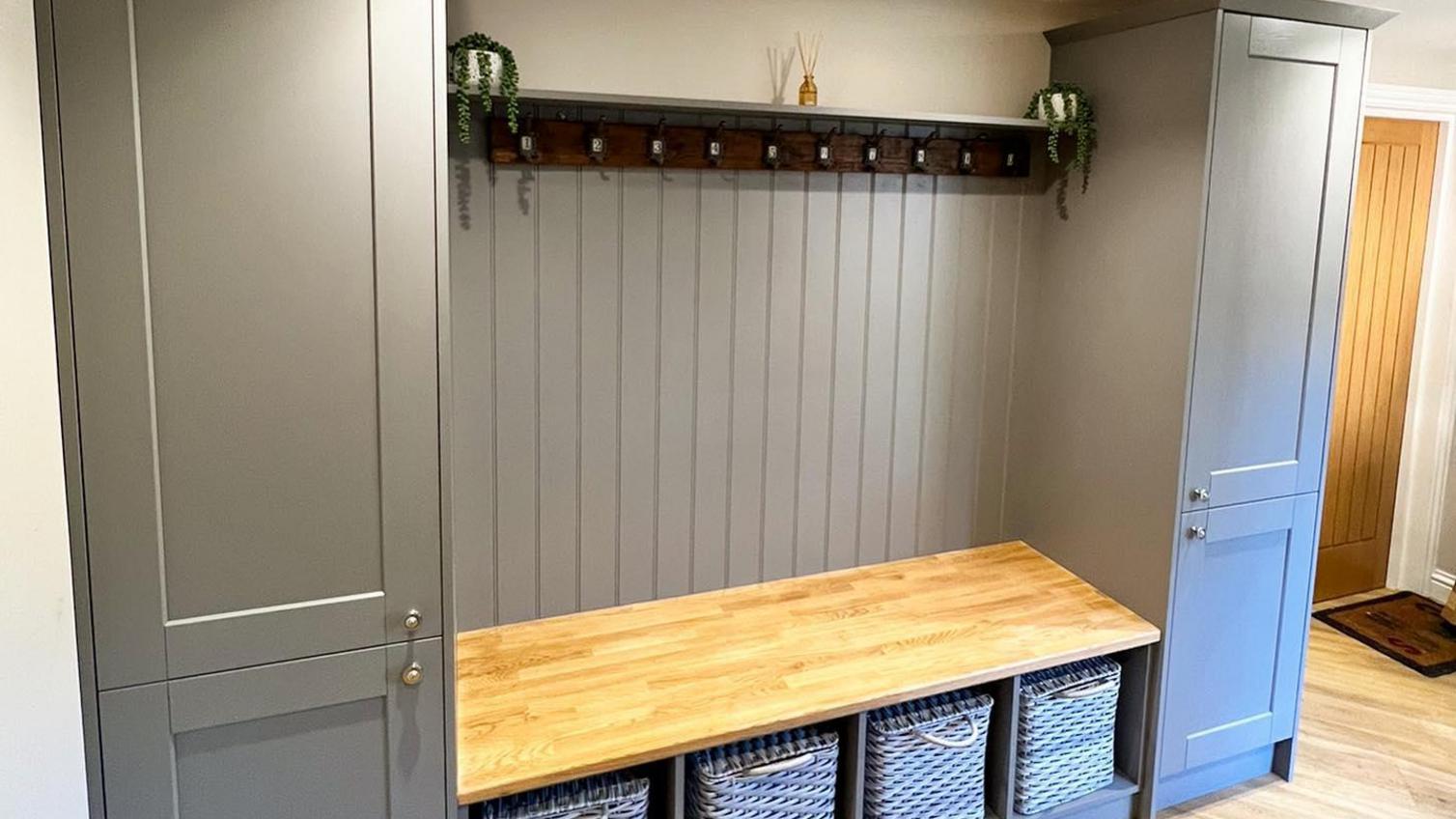 Fairford dusk blue larder cabinets in a hallway with an end panel underneath coat hooks and behind a bench.