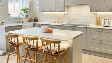 L-shaped kitchen with an island, from the Chelford Pebble range. It has chrome cup handles and a bespoke Silestone worktop.
