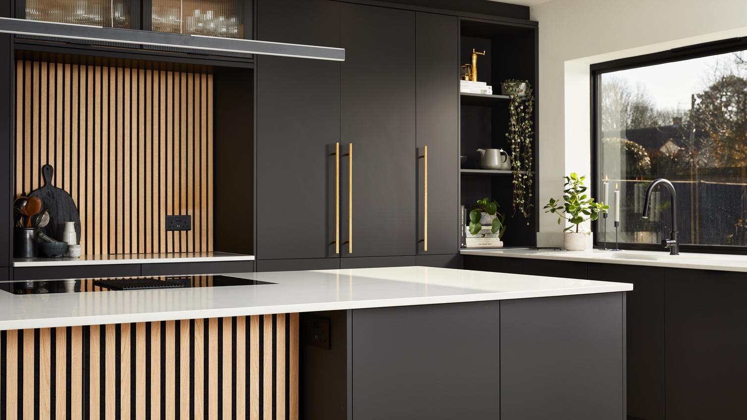 Howdens 2022 Kitchen Of The Year Winner's kitchen which includes black slab cupboard doors, oak panels, and white worktops.