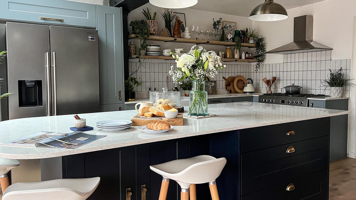 Two-tone shaker kitchen with dusk blue wall units and a navy island, with antique brass handles and white worktops.