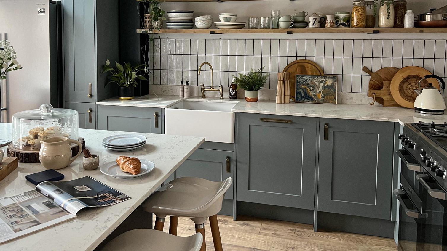 Dusk blue shaker kitchen with an island, white quartz worktop, open wood shelving, and kitchen accessories.